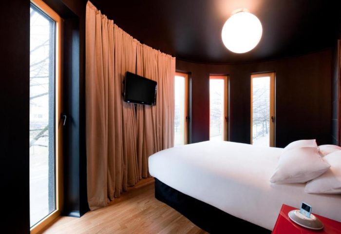 Bedroom at Axel Hotel Berlin, a gay-friendly hotel. Modern design with dark walls, wood floors, and large windows. Bed with white linens, TV, and curtains.
