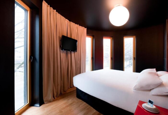 Bedroom at Axel Hotel Berlin, a gay-friendly hotel. Modern design with dark walls, wood floors, and large windows. Bed with white linens, TV, and curtains.