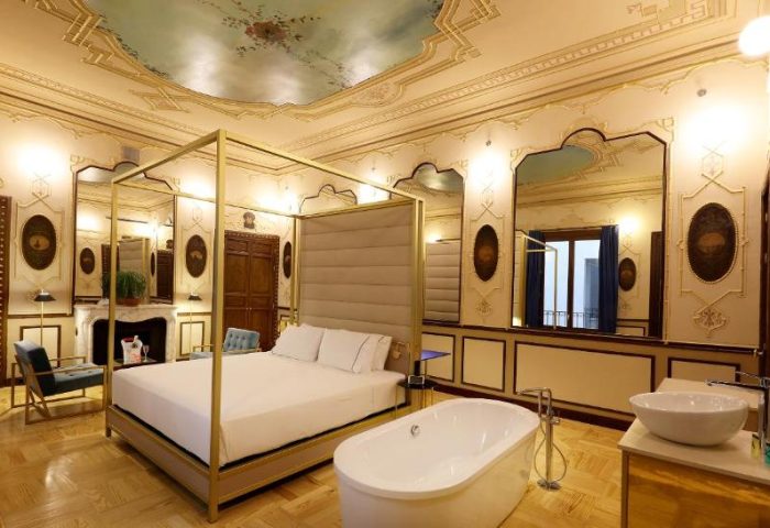 Luxury suite at Axel Hotel Madrid, an adults-only, gay-friendly hotel. Features a four-poster bed, bathtub, and ornate ceiling.