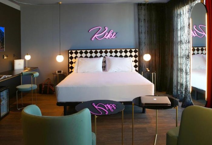 Axel Hotel Madrid adults-only room. Gay-friendly hotel with double bed, neon sign, desk, and chairs. Modern, stylish design.