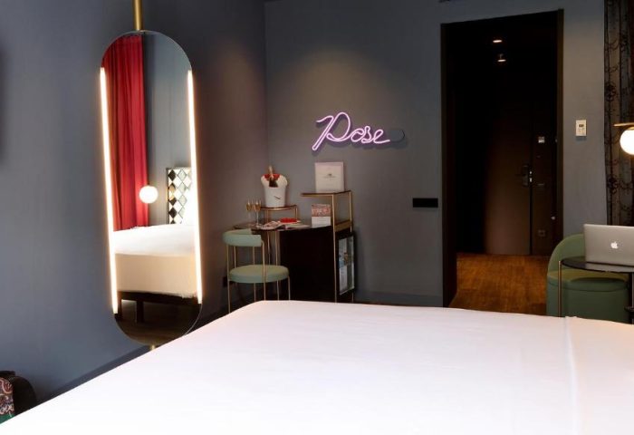 Axel Hotel Madrid adults-only room. Modern design with a large mirror, neon Pose sign, and a minibar. Gay-friendly hotel interior.