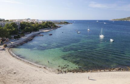 Beach view from AxelBeach Ibiza, a gay-friendly, adults-only hotel. Clear turquoise water, boats, and sandy beach for gay travel.