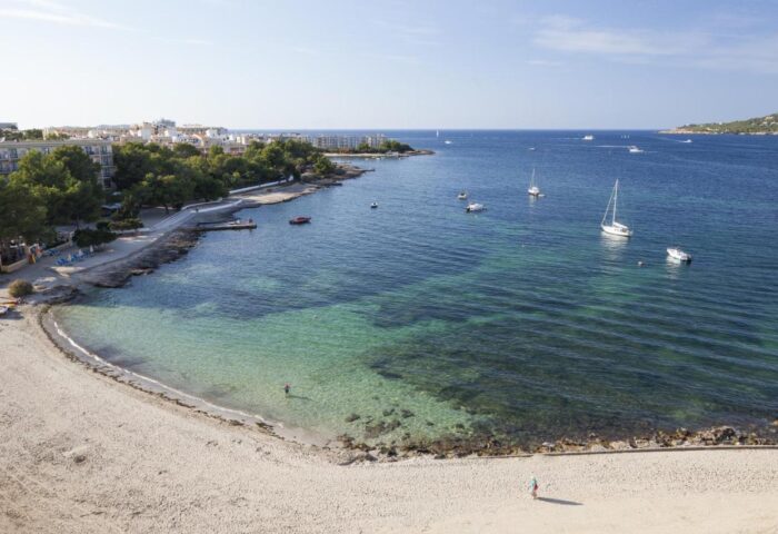 Beach view from AxelBeach Ibiza, a gay-friendly, adults-only hotel. Clear turquoise water, boats, and sandy beach for gay travel.