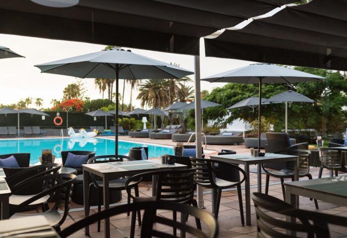 AxelBeach Maspalomas ApartLounge Club-Only Adults: Poolside dining area with tables, chairs, umbrellas, and lounge chairs. Gay-friendly hotel.