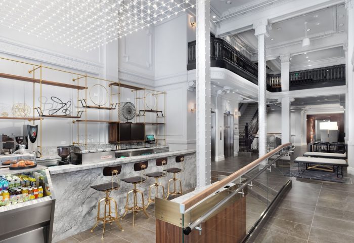 Axiom Hotel's lobby, a gay-friendly hotel. Bar with marble countertop and gold stools. Modern design, open space, and stylish decor.