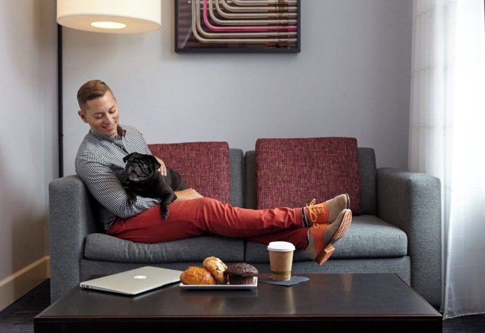 Gay-friendly Axiom Hotel: Man relaxing on a sofa with a pug. A laptop, coffee, and pastries are on the table. Pet-friendly hotel.