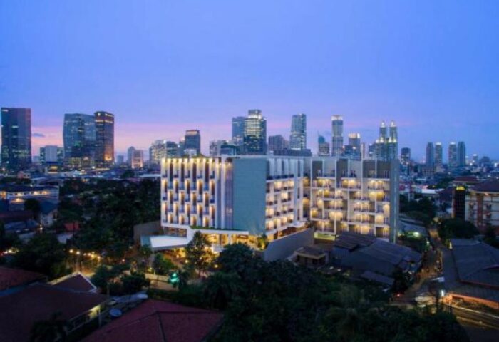 Ayaka Suites, a gay-friendly hotel. Exterior view of the hotel at dusk, with the city skyline in the background. Modern architecture.