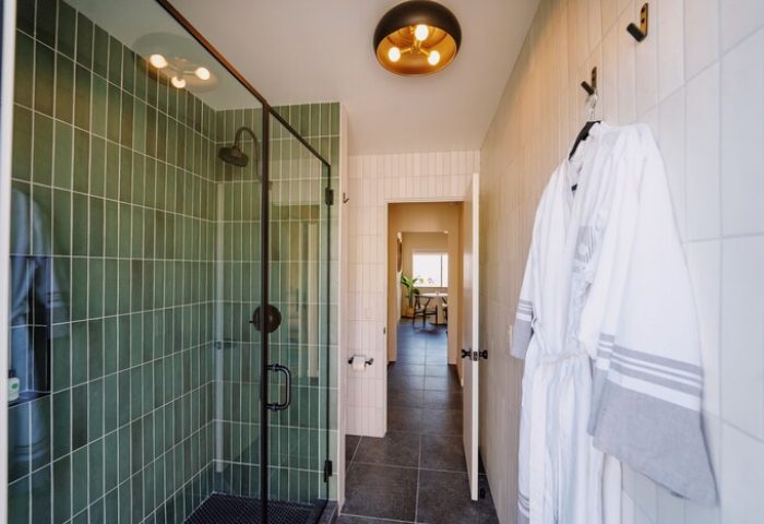 Azure Sky Hotel adults-only bathroom with green tiled shower, robe, and modern light fixture. Gay-friendly hotel interior design.