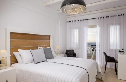 Azzurro Suites gay-friendly hotel room. Minimalist bedroom with white bedding, wood headboard, and balcony view. Modern, stylish gay travel.