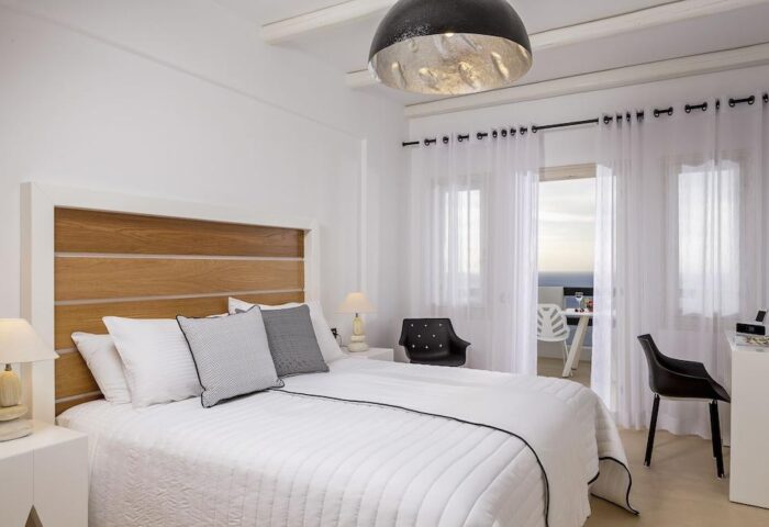 Azzurro Suites gay-friendly hotel room. Minimalist bedroom with white bedding, wood headboard, and balcony view. Modern, stylish gay travel.