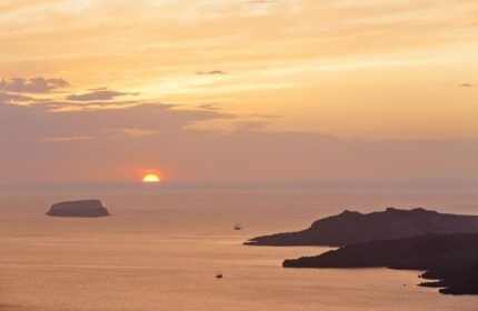 Sunset view from Azzurro Suites, a gay-friendly hotel. Islands and boats dot the sea under a golden sky. Perfect for gay travel adventures.
