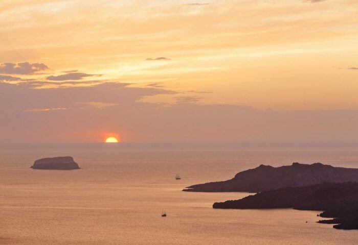Sunset view from Azzurro Suites, a gay-friendly hotel. Islands and boats dot the sea under a golden sky. Perfect for gay travel adventures.