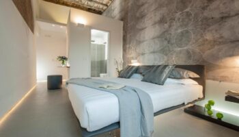 Gay-friendly hotel B&B second-floor room. Modern design with a gray patterned wall. King bed with white linens and gray pillows. Bathroom view.