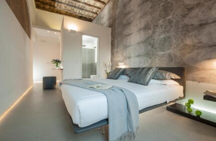 Gay-friendly hotel B&B second-floor room. Modern design with a gray patterned wall. King bed with white linens and gray pillows. Bathroom view.