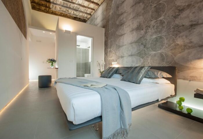 Gay-friendly hotel B&B second-floor room. Modern design with a gray patterned wall. King bed with white linens and gray pillows. Bathroom view.