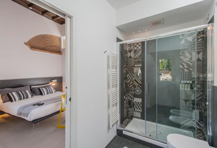 B&B First Floor: Gay-friendly hotel room with a shower and view of the bedroom. The shower has patterned tiles and glass doors. Modern design.