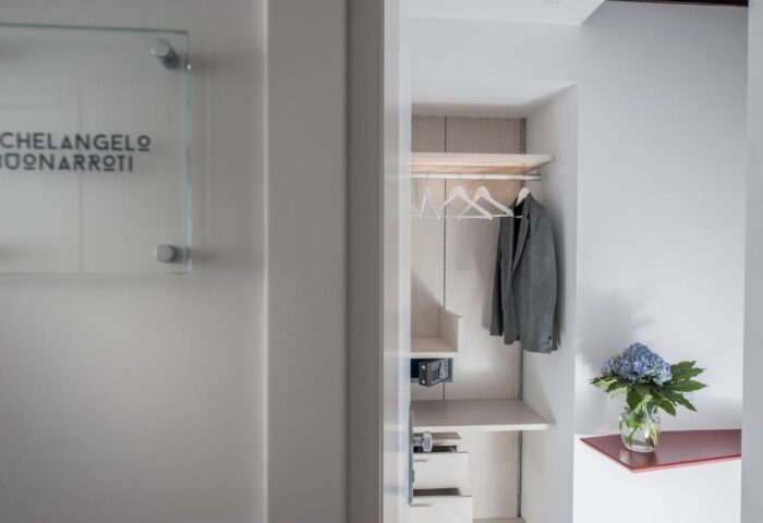 B&B First Floor gay-friendly hotel closet. Open closet with safe, drawers, jacket, hangers, and flowers in a vase. Michelangelo Buonarroti sign.