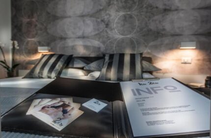 Gay-friendly hotel B&B second floor room. Bed with striped pillows, info booklet, and promotional material. Modern design.