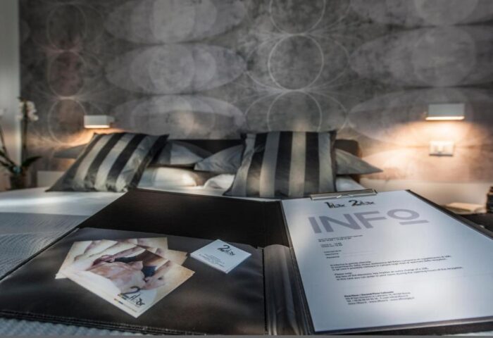 Gay-friendly hotel B&B second floor room. Bed with striped pillows, info booklet, and promotional material. Modern design.