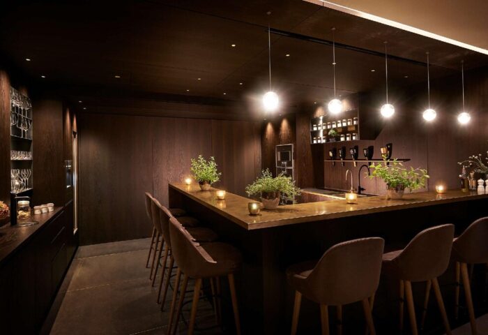 BEYOND by Geisel, a gay-friendly hotel. Dark wood bar with stools, plants, and soft lighting. Upscale travel for gay men.