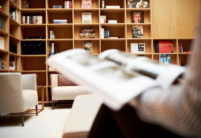 BEYOND by Geisel gay-friendly hotel: Person reading in a cozy lounge area with a large bookshelf. A relaxing space for gay travelers.