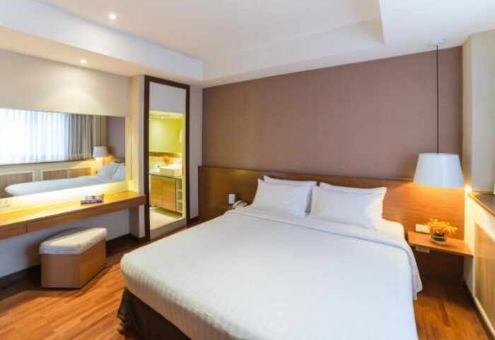 Bandara Suites Silom gay-friendly hotel room. Modern interior with white bedding, desk, and bathroom view. Comfortable stay in Bangkok.