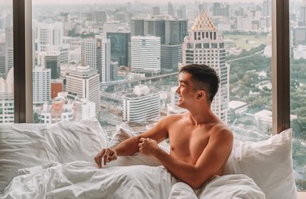 Gay man at Banyan Tree Bangkok, a gay-friendly hotel. Topless man in bed with city view. Bangkok hotel for gay travelers.