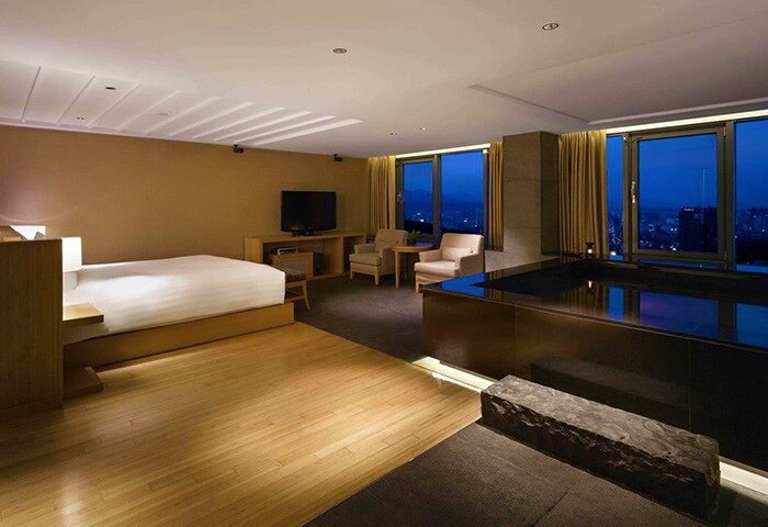 Banyan Tree Club & Spa Seoul room. Gay-friendly hotel with a bed, chairs, and a tub overlooking the city at night. Luxury travel.