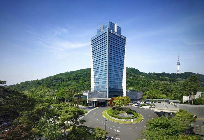 Banyan Tree Club & Spa Seoul. Gay-friendly hotel exterior view. Modern architecture, lush greenery, and Seoul Tower in the background.