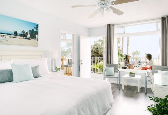 Bayside Hotel room with balcony view. Two women chat on the balcony. Gay-friendly hotel with beach access. Coastal decor, light & airy.