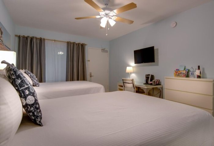 Bayside Hotel guest room with two beds, desk, TV, and ceiling fan. Gay-friendly hotel room interior. Comfortable lodging for gay travelers.