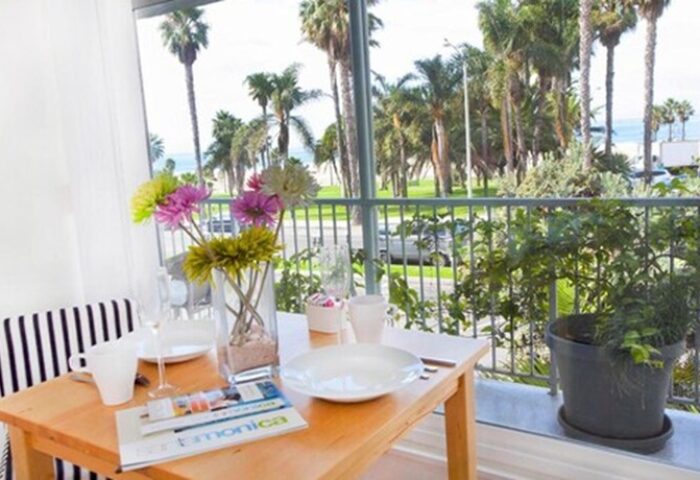 Bayside Hotel balcony view. Table set for breakfast with flowers. Gay-friendly hotel with ocean view. Palm trees visible. Santa Monica travel.