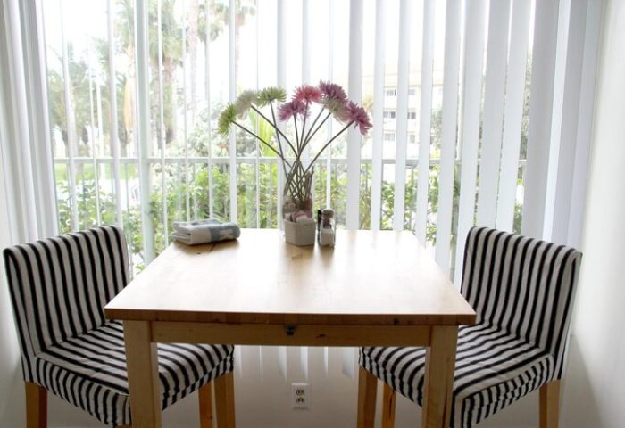 Dining area at Bayside Hotel, a gay-friendly hotel. Table with striped chairs, flowers, and a view of palm trees. Gay travel lodging.