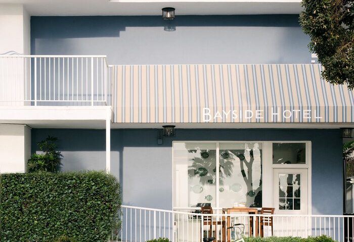 Facade of Bayside Hotel, a gay-friendly hotel. A bicycle stands outside the entrance with a striped awning. Ideal for gay travel.
