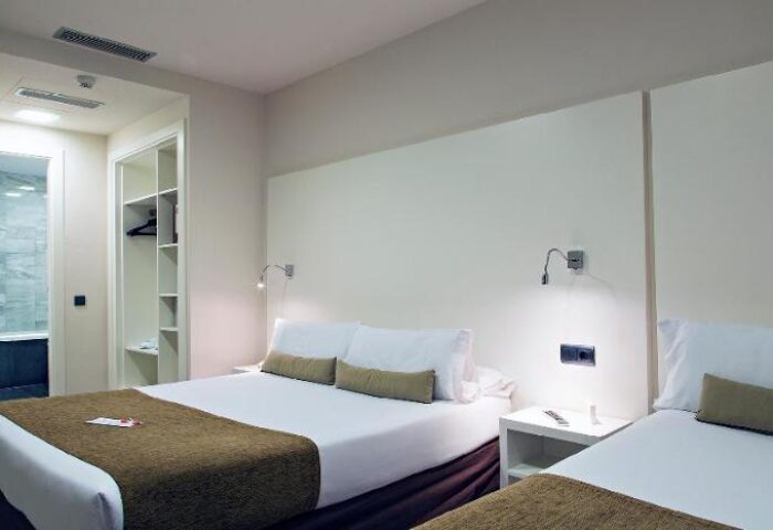 BCN Urbany Hotels Del Comte gay-friendly hotel room. Two beds, white linens, brown throws, bedside table, closet, and bathroom.