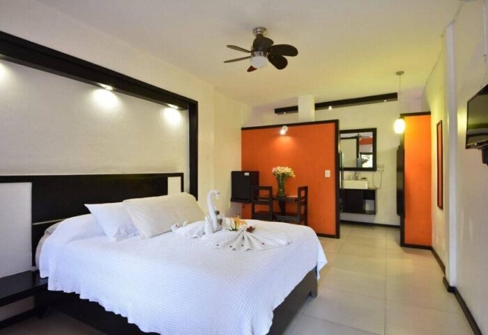 Beach Energy Hotel by BFH: Gay-friendly hotel room interior. Bed with swan towels, orange accent wall, and open bathroom. Modern design.
