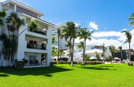 Beachscape Kin Ha Villas & Suites Cancun: Gay-friendly hotel with lush green lawn, palm trees, and white buildings under a blue sky.