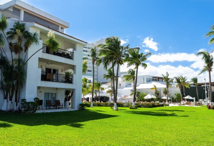 Beachscape Kin Ha Villas & Suites Cancun: Gay-friendly hotel with lush green lawn, palm trees, and white buildings under a blue sky.