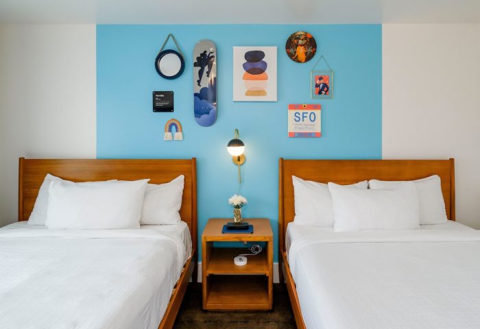 Beck's Motor Lodge: Gay-friendly hotel room with two beds, blue accent wall, and colorful skateboard art. A unique travel experience.