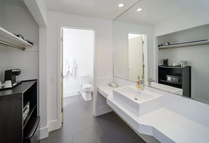 Beck's Motor Lodge gay-friendly hotel bathroom. Modern white sink, large mirror, and open doorway to the toilet. Dark gray tiled floor.