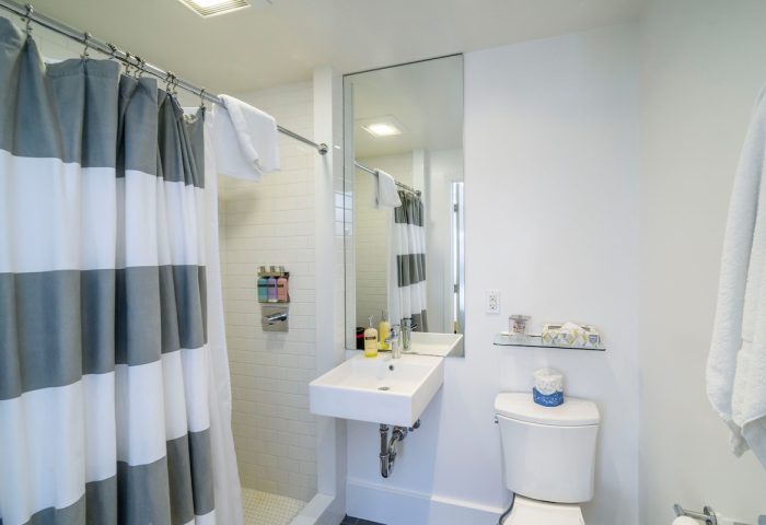 Bathroom at Beck's Motor Lodge, a gay-friendly hotel. Shower with striped curtain, sink, toilet, and mirror. Modern, clean design.