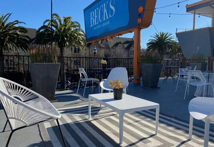 Beck's Motor Lodge outdoor patio, a gay-friendly hotel. Lounge seating, palm trees, and a retro sign create a welcoming space. Perfect for gay travel.