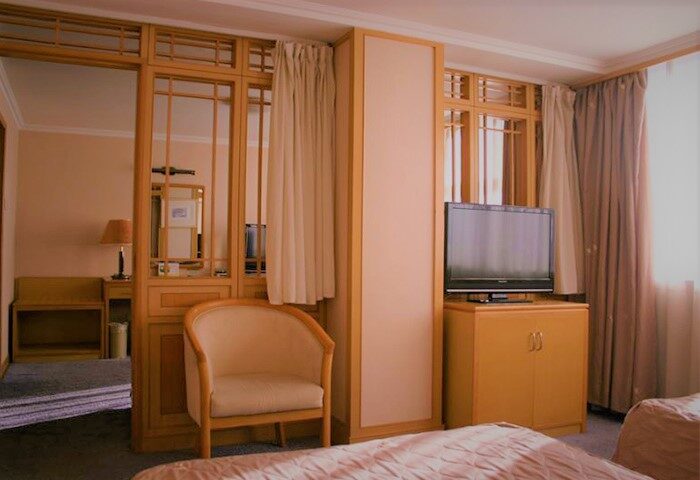 Beijing Guoan Hotel room. Gay-friendly hotel with a chair, TV, and doorway to another room. Modern, comfortable accommodations.