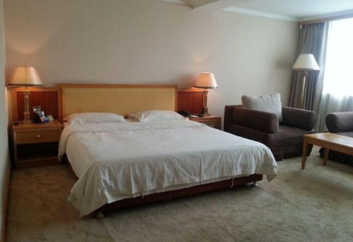 Bedroom in Beijing Guoan Hotel, a gay-friendly hotel. Queen bed with white linens, brown sofa, lamps, and carpet. Travel advice for gay men.