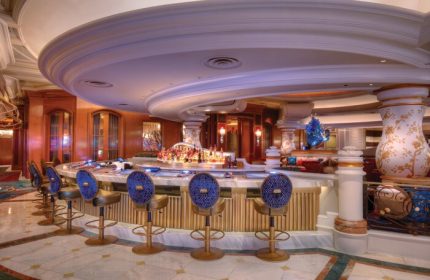 Interior of the gay-friendly Bellagio Hotel bar. The bar has a round shape and is decorated with blue chairs and marble countertops.