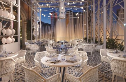 Gay-friendly Bellagio Hotel restaurant with fountain view. Elegant dining area with white wicker chairs, tables set for dinner. Fine dining.