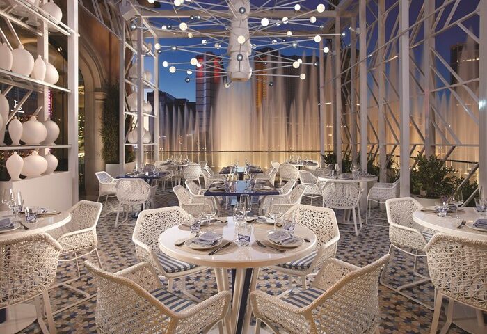 Gay-friendly Bellagio Hotel restaurant with fountain view. Elegant dining area with white wicker chairs, tables set for dinner. Fine dining.