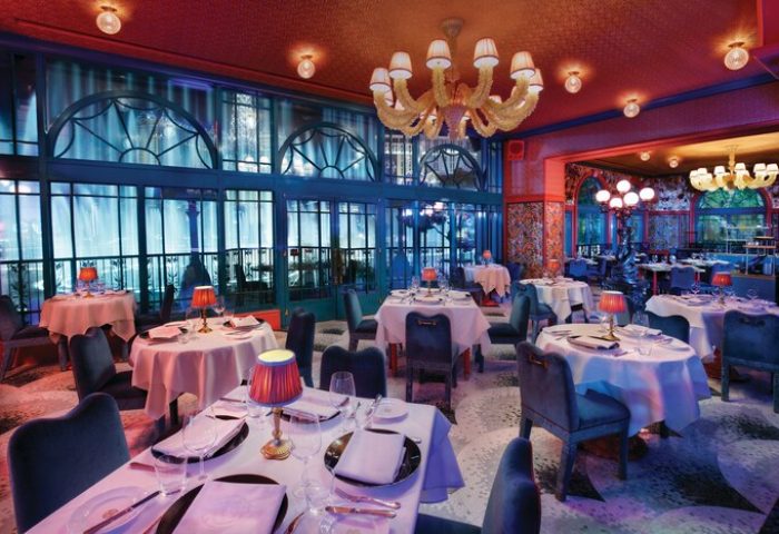 Elegant dining room at the gay-friendly Bellagio Hotel. Tables set with white linens, chandeliers, and large windows. Upscale ambiance.