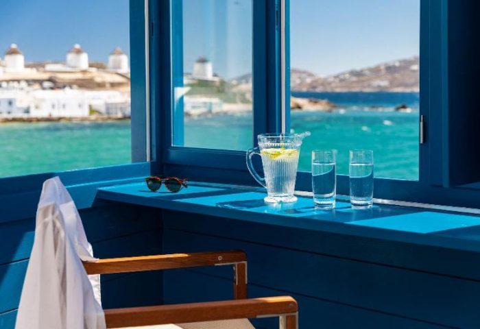 Belvedere Little Venice pied-a-terres view. Gay-friendly hotel room with water, sunglasses, and sea view. Mykonos windmills in the background.