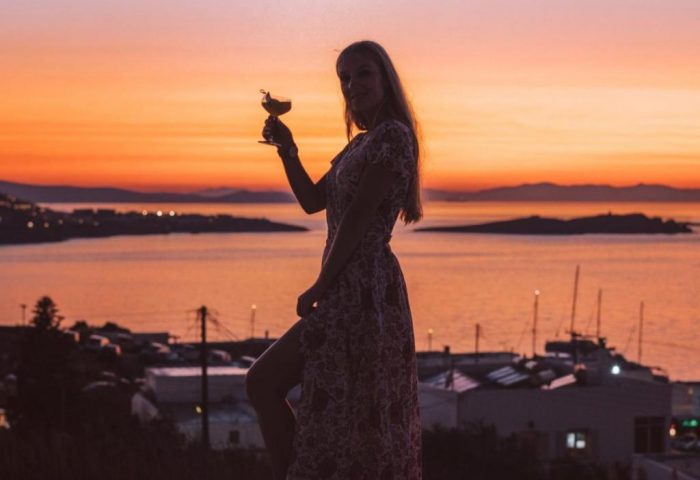 Sunset at Gay-Friendly Hotel Belvedere Mykonos. Woman with cocktail at Hilltop Complex, enjoying the view. Mykonos travel advice for gay men.